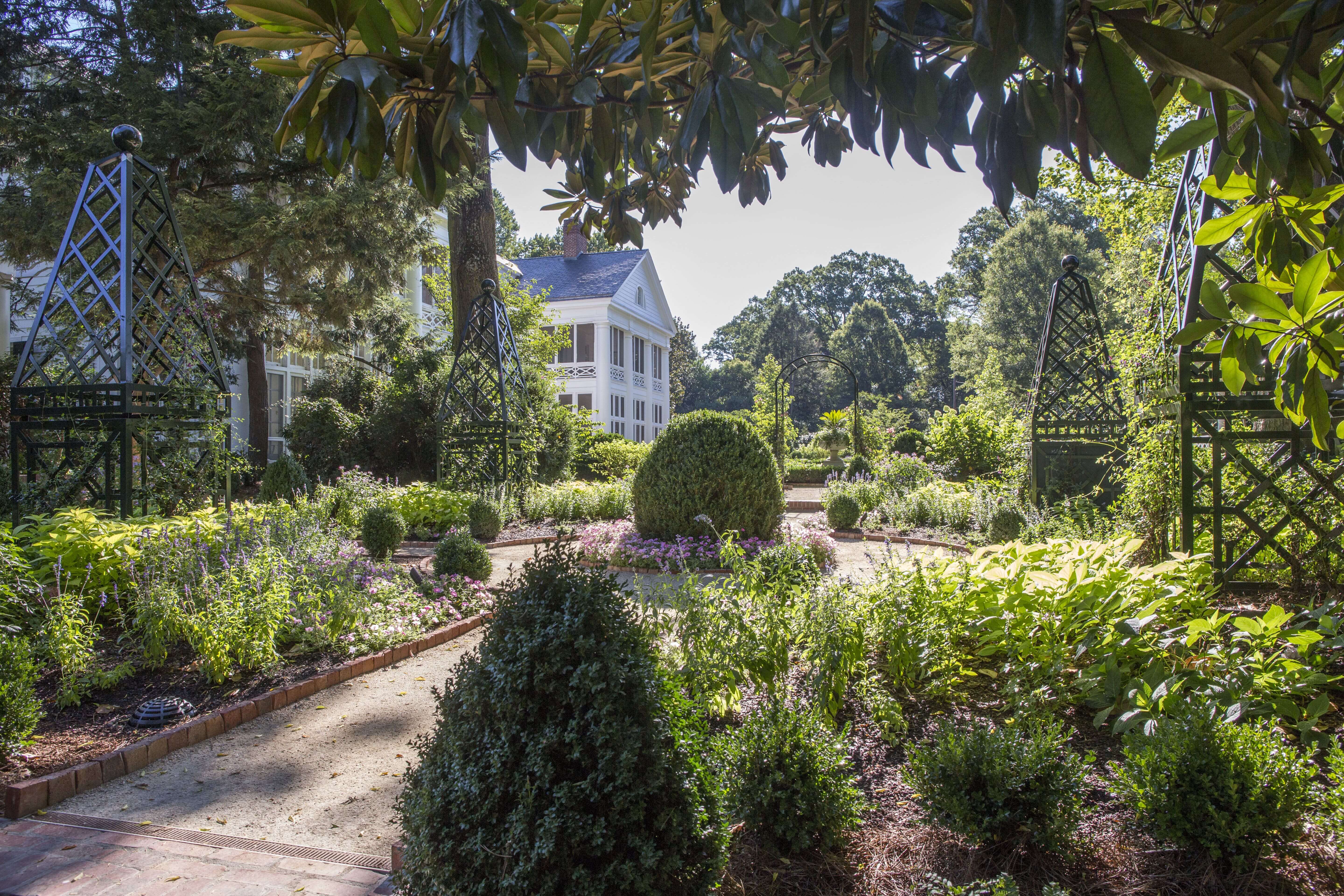 A well-manicured garden with a pathway leading to a large white house.
