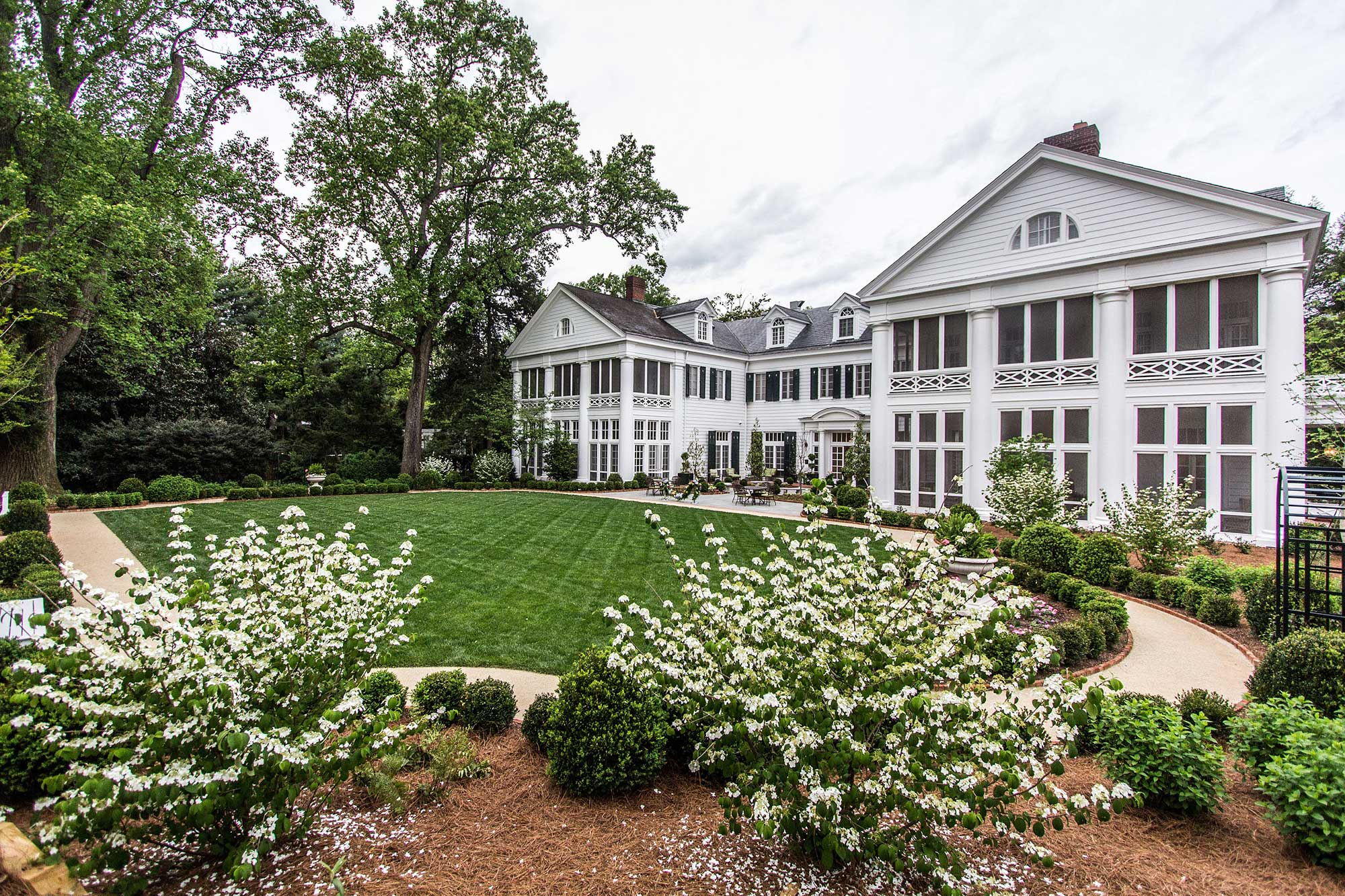 A large white mansion with a well-manicured lawn and garden beds.